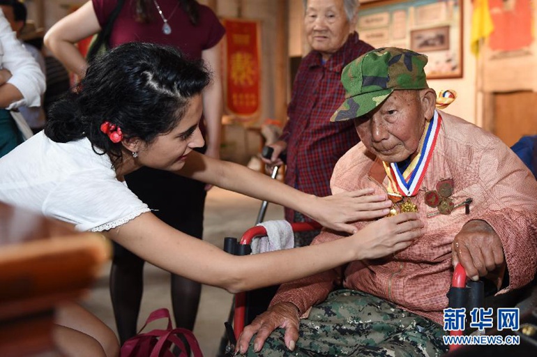  玛丽亚（左）参加在浙江省金华市汤溪镇寺平村的古祠堂内的重阳节敬老活动，为92岁的抗战老兵戴汝才整理勋章（10月21日摄）。玛丽亚说，看到老人，她想起了自己同样90多岁的爷爷。