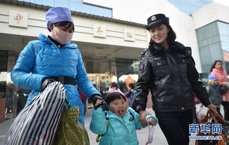 1月26日，田小凤（右）在车站帮助一位带小孩的乘客进站登车。