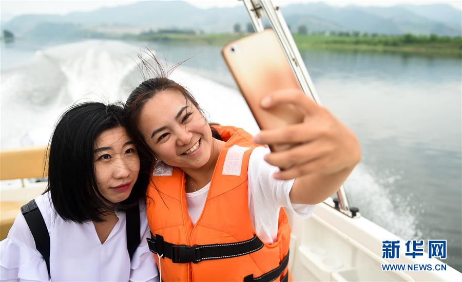 6月21日,两名乘坐游艇观赏鸭绿江上风光的游客在自拍。